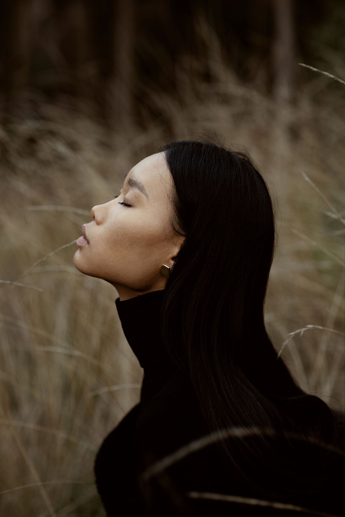 Portrait of a model wearing handmade earrings and a black turtle neck in a gold field. Photographed by Filianna Karamanli.