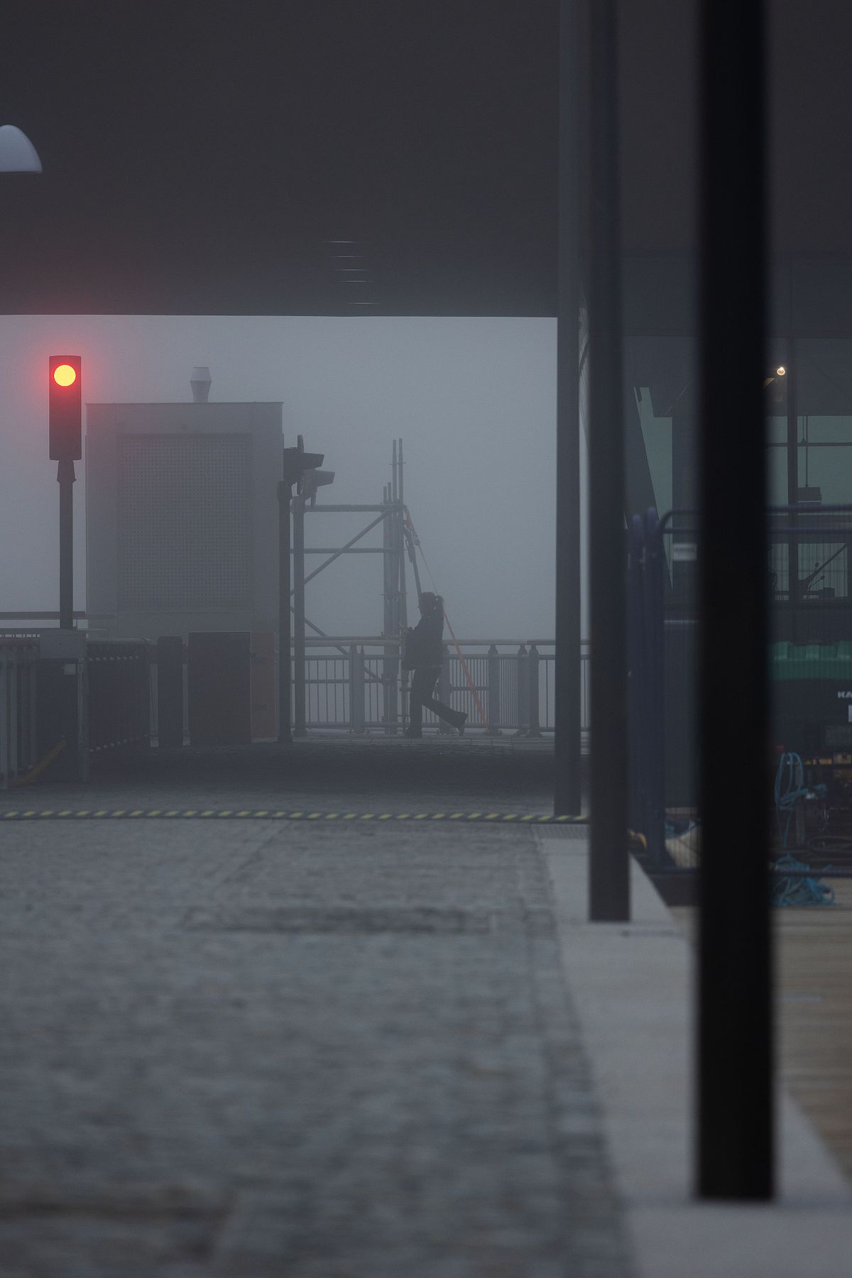 Siluett av person vid kaj i t&auml;t dimma med r&ouml;tt ljus i f&ouml;rgrunden