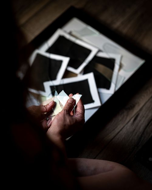 Hands reaching out to hold broken glass that rest on blackened photos.