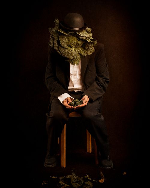 photo tarot Homme à Tête de Chou, homme assis tenant des feuilles de chou, visage transformé, évocation du temps qui passe
