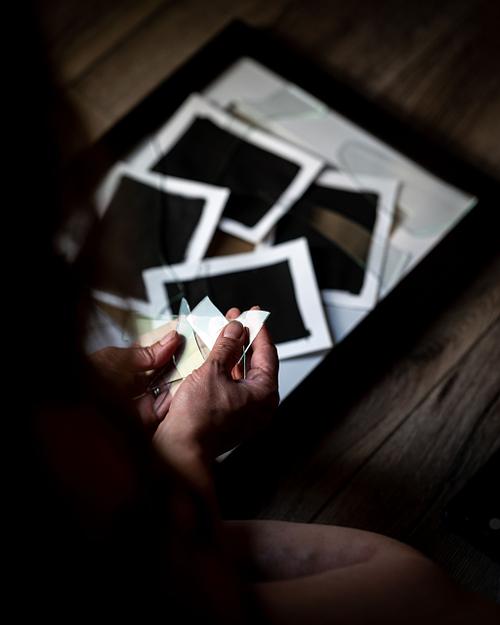 Hands reaching out to hold broken glass that rest on blackened photos.