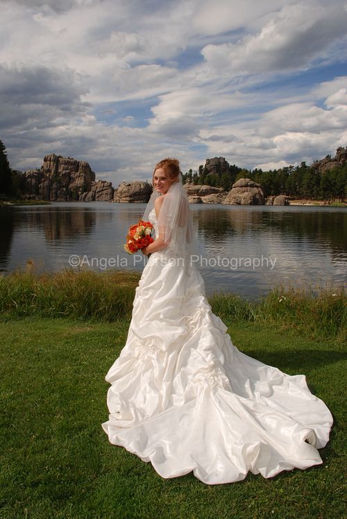 A bride hold her bouquet and stands in front of Sylvan Lake with thick clouds above