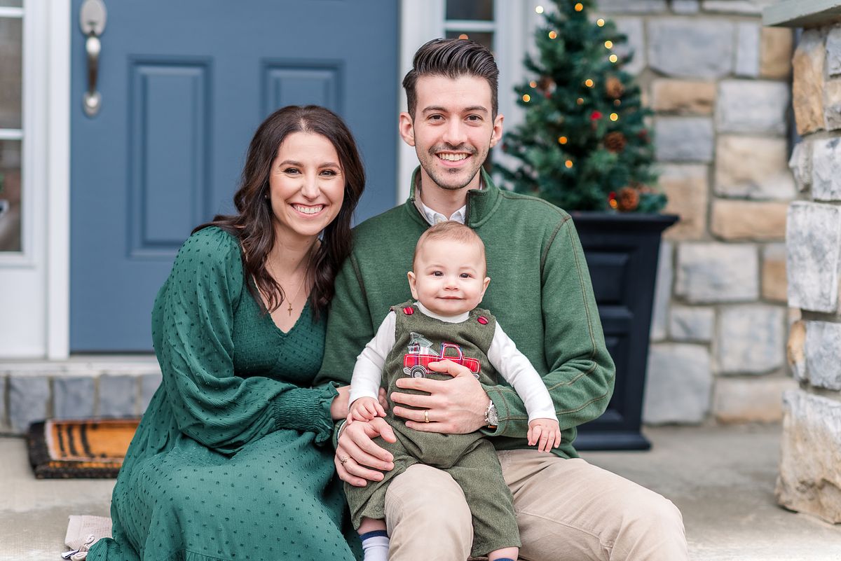 Family of three sitting on their porch with small Christmas tree behind them with Cranberry Township, PA newborn photographer