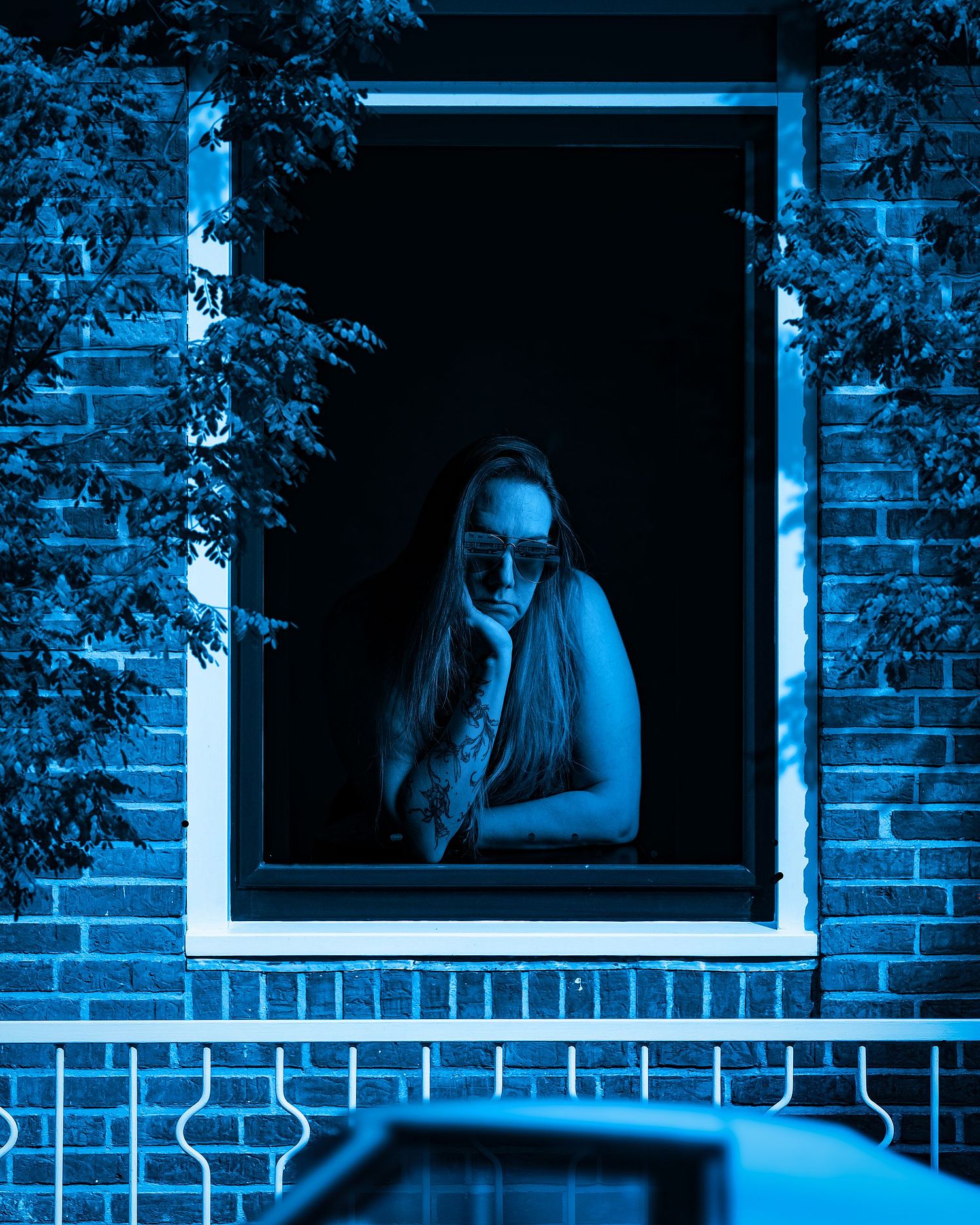 A blue scene of a woman wearing shades looking out the window a blue car.